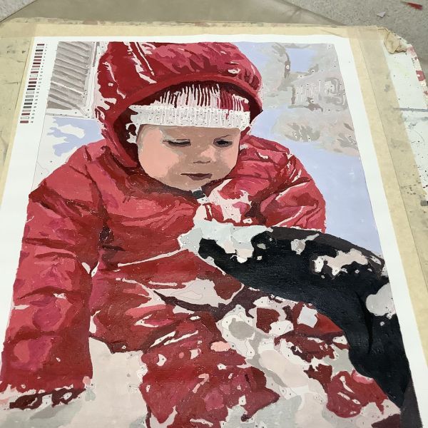 Almost completed custom paint by numbers kit of a baby in red jacket.